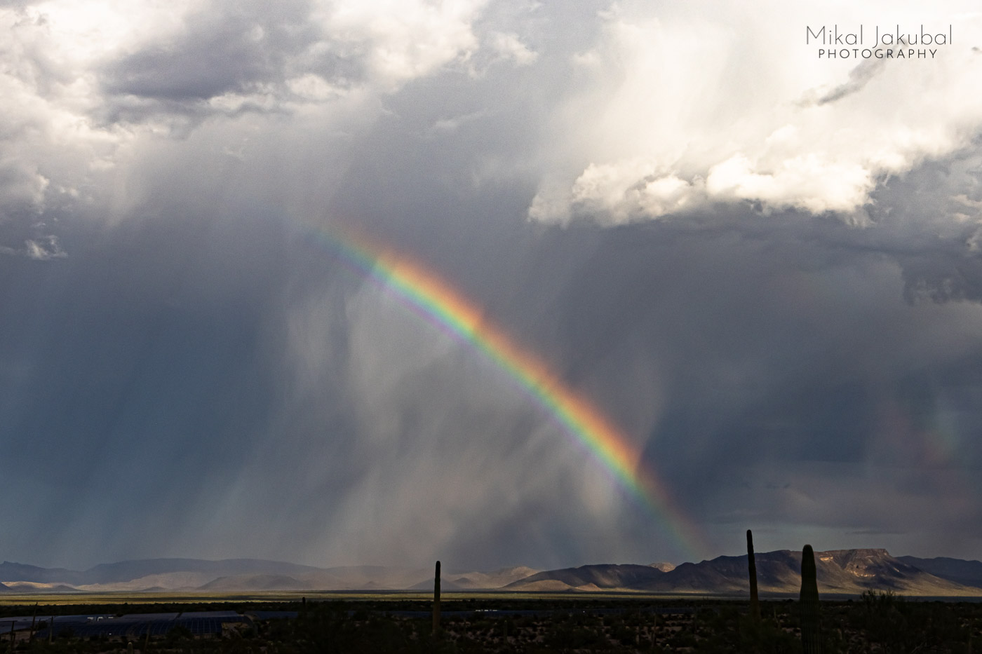 A rainbow arched down into the desert below white and gray storm clouds.
