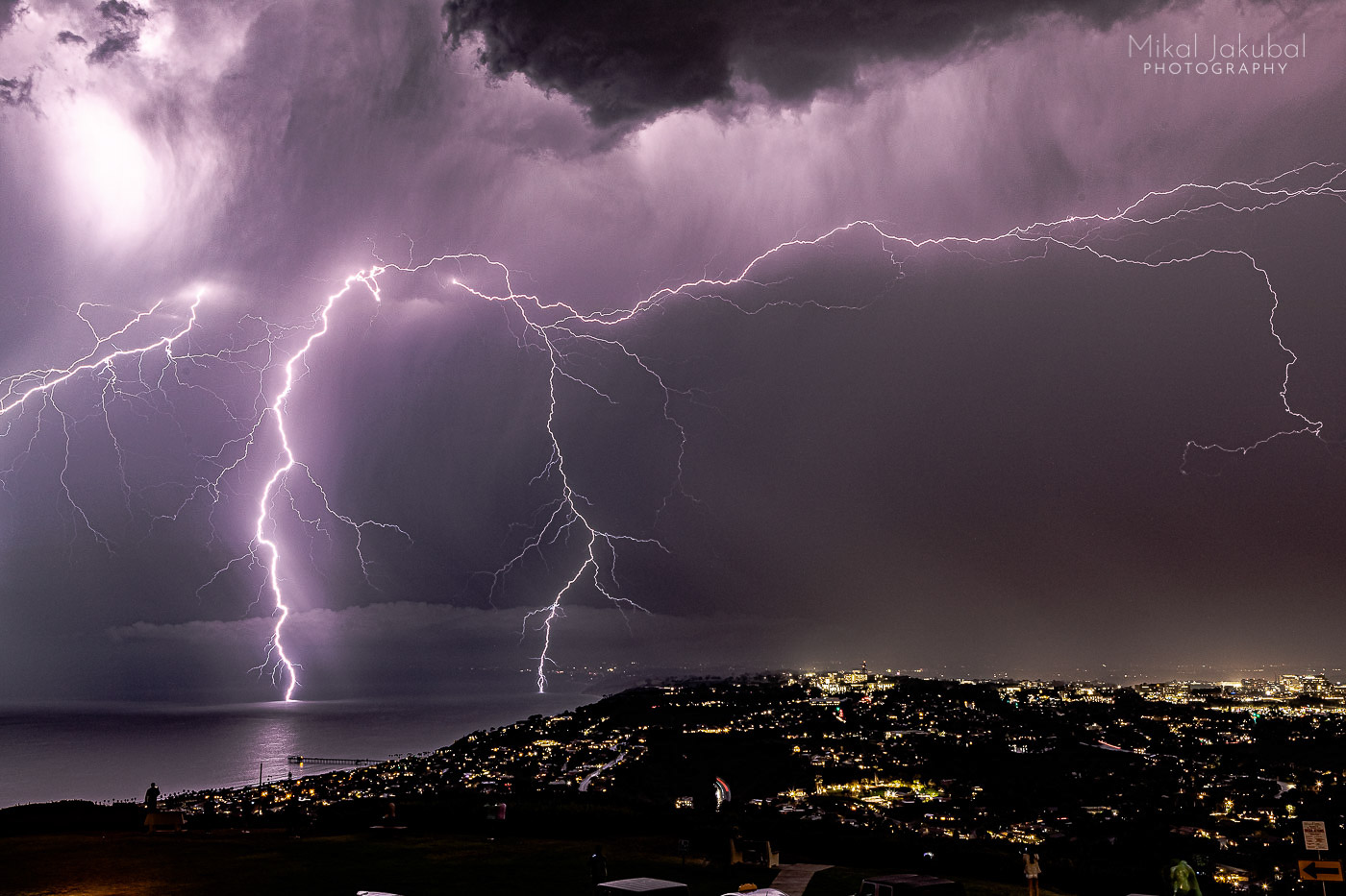 Two purple lightning bolts strike the Pacific Ocean just off the beach from San Diego at night.