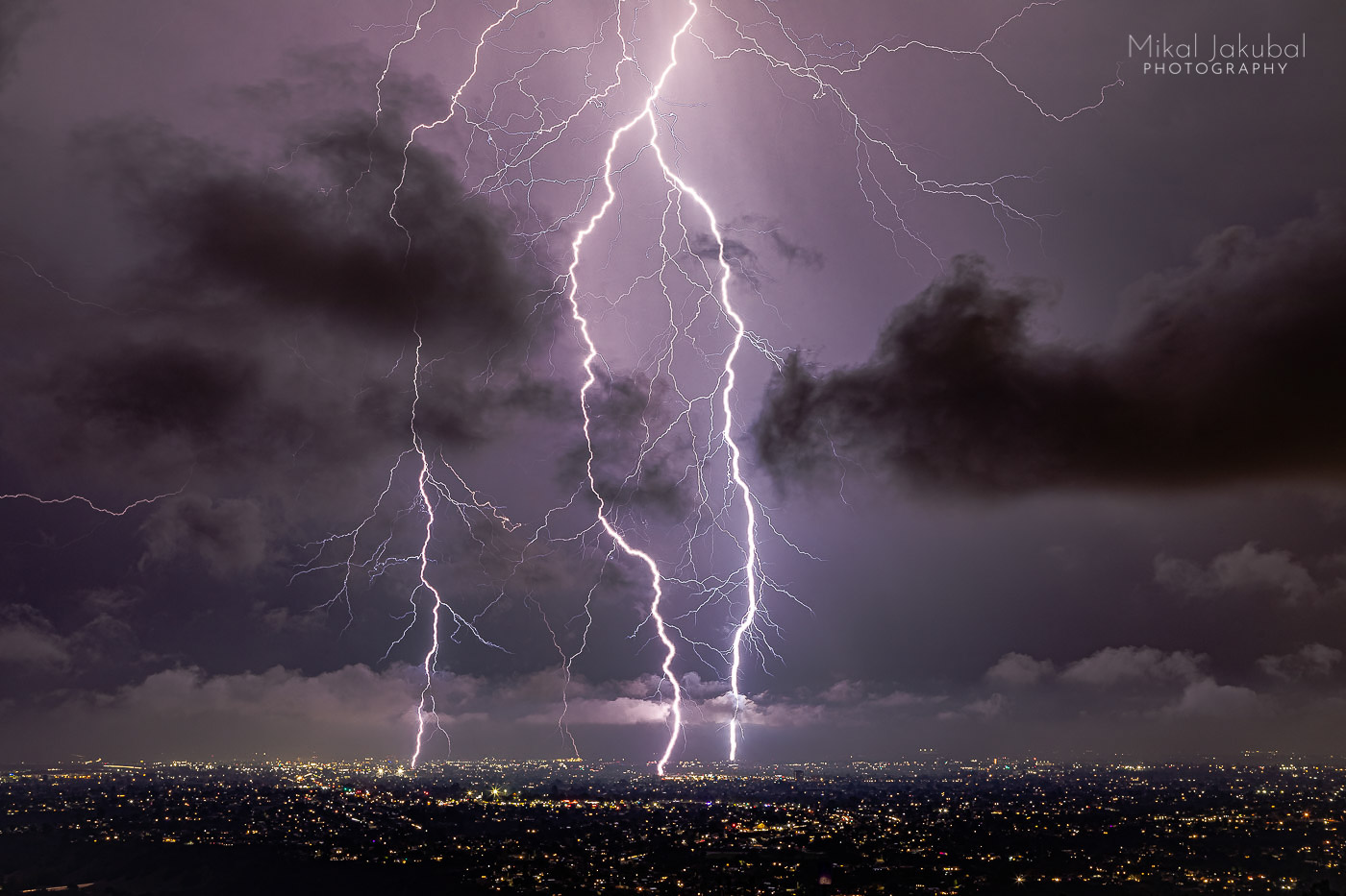 Three gigantic purple lightning bolts drop vertically down onto the city of San Diego at night.