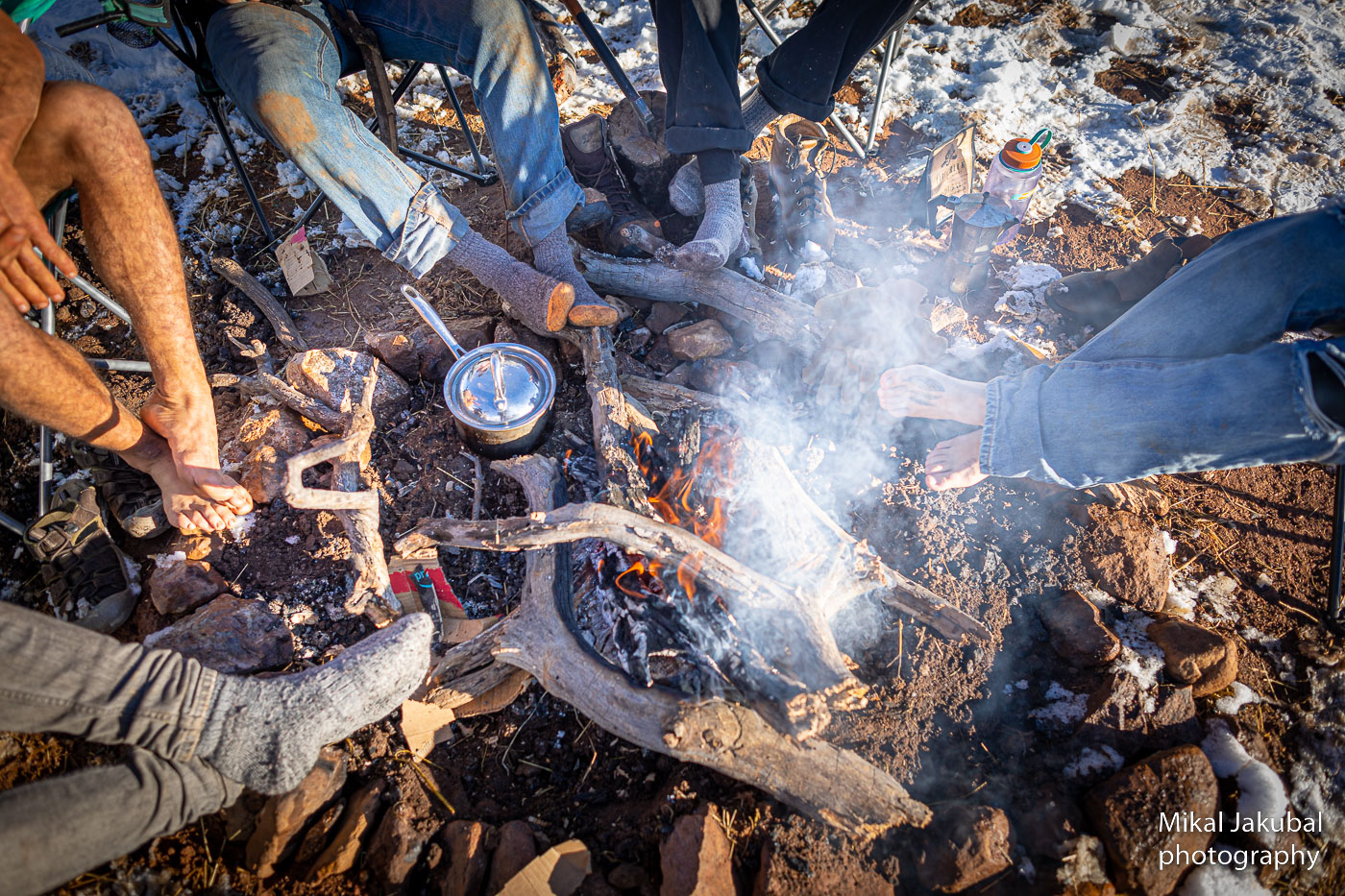 A small campfire from above. Five sets of legs and feet are seen from above as people warm their feet.