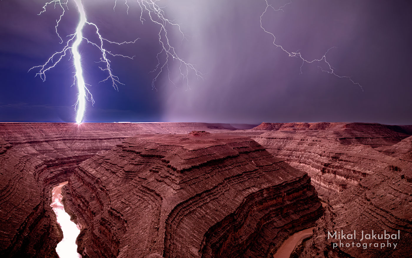 A night shot of a gigantic lightning bolt hitting the rim of a serpentine redrock canyon with a muddy brown river in the bottom.