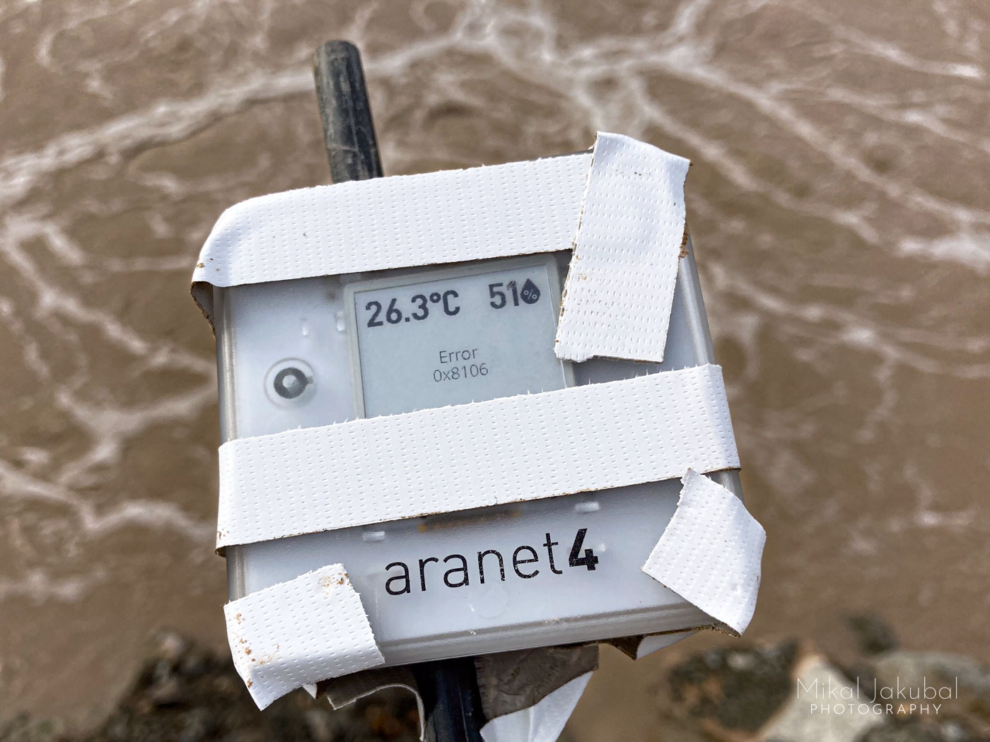 A hand held CO2 meter made of milky white plastic about 3" x 3" showing an "Error" message on the screen. It is taped with strips of white tape to the end of a fiberglass tent pole. Below in the background is the brown bubbling surface of the pool.